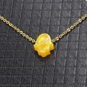 Macro shot of gold necklace with orange Hamsa hand opal pendant on black leather