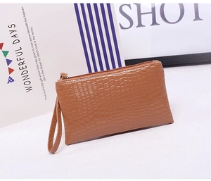 Detailed side view of a brown crocodile pattern leather wristlet bag with metal zipper