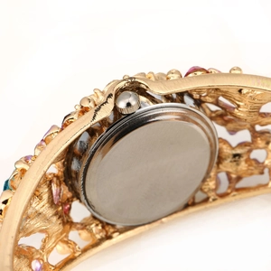 Macro shot of vintage gold flower bangle watch showing silver case back and colored gems