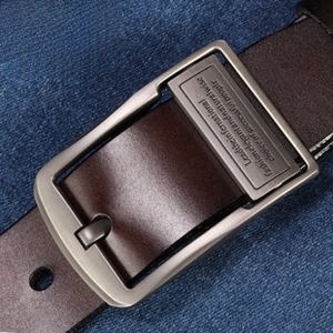 Detail of dark brown leather belt featuring a brushed silver metal pin buckle on denim