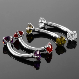 Close-up of curved stainless steel eyebrow rings with multi-color zircon stone settings