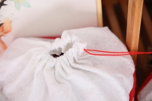 Detail view of white non-woven Christmas gift bag showing double drawstring closure texture