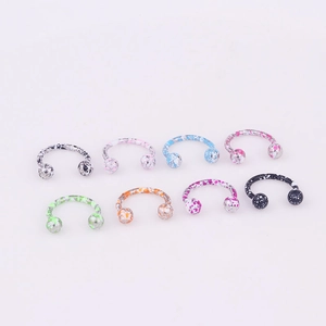 Macro shot of 8-color splatter painted stainless steel horseshoe nose rings on pink background