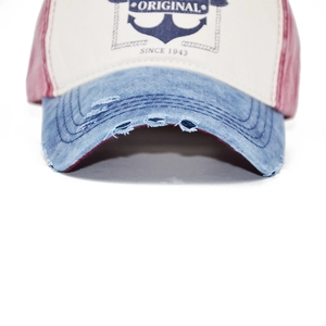 Close-up of distressed denim brim with frayed edges and embroidered anchor logo on cap