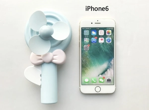 Manual candy-colored hand-press fan with bow detail next to phone for size comparison