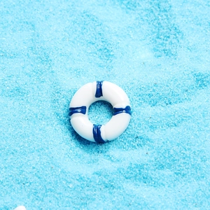 Macro view of a white and blue resin lifebuoy ornament on a blue sand background