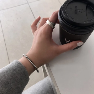 Close-up of a silver rope chain bangle and minimalist cross ring held with a coffee cup