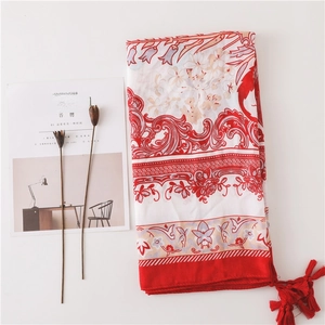 Détail d'une écharpe à fleurs rouges et blanches avec pompons sur tissu en lin