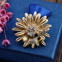 Close-up of golden bee and daisy brooch with crystals on a navy blue gift box