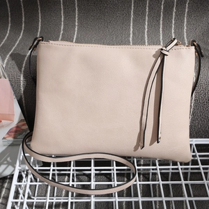 Detail of beige textured faux leather crossbody bag with gold zipper and stylish tassels