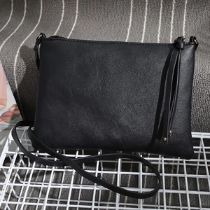 Detail of black leather crossbody bag with tassel and adjustable strap on a grid rack