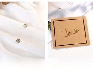 Close-up of gold Evil Eye stud earrings with blue and white zircons on a textured background