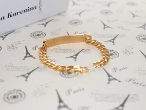 Detailed view of a gold-plated Cuban chain bracelet with ID tag on vintage Paris paper