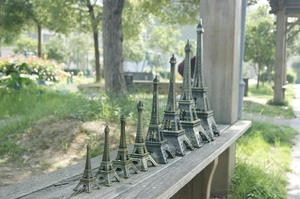 Collezione di miniature in metallo della Torre Eiffel in varie dimensioni su una panchina