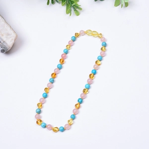 Collier pour bébé en ambre naturel et quartz rose avec perles sur fond blanc épuré