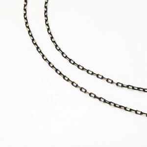 Detail of metal eyeglass chain in black and gold finish with textured link structure