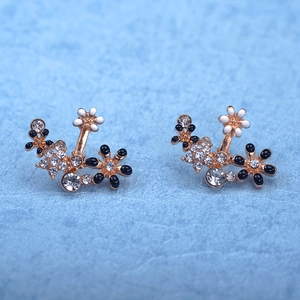 Macro shot of floral crystal earrings featuring white and black petals on gold alloy base