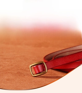 Detail of red leather skinny belt featuring a polished gold rectangular alloy buckle