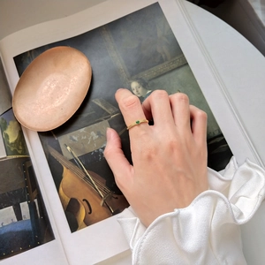 Artistic close-up of a vintage-style gold ring with a green gemstone on a model's hand