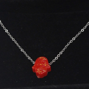 Macro view of silver chain with red synthetic opal Hamsa hand pendant on black velvet