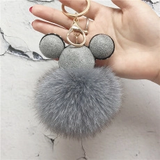 Detail shot of a grey faux fur pompom keychain with sequined Mickey ears and gold hardware