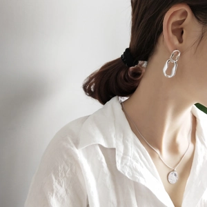 Close-up of geometric silver chain earrings and round pendant necklace on a model