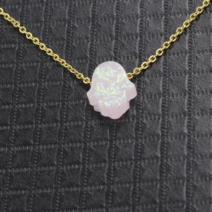 Close-up of golden necklace with iridescent white opal Hamsa hand charm on dark surface