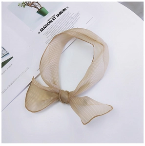 Gros plan d'un foulard en mousseline beige à pois noué sur un magazine français