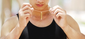 Golden bullet-shaped pendant necklace on a model shown in a bright outdoor setting
