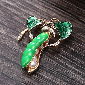 Fashionable golden pea pod brooch with green enamel leaves and white pearls on wood