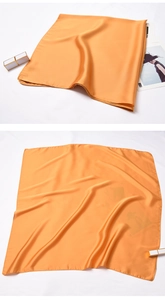 Macro detail of glossy golden square silk scarf with smooth texture and hemmed edges