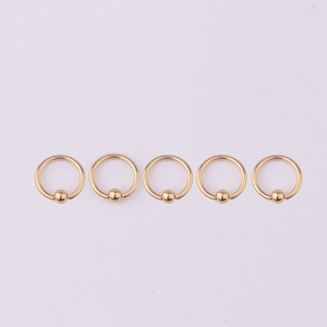 Five gold 316L stainless steel captive bead rings for body piercing on pink background