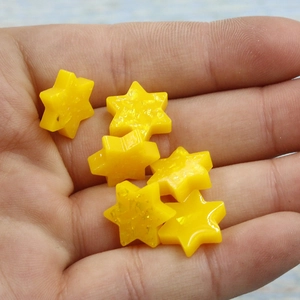 Macro shot of five yellow star-shaped resin charms held in hand for size reference