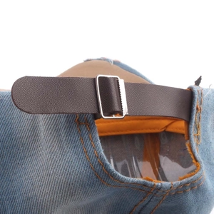Detail of adjustable brown faux leather strap and metal buckle on denim baseball cap