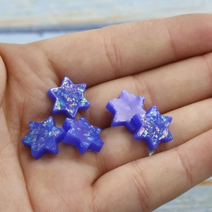 Macro detail of five translucent purple resin star charms with iridescent glitter in hand
