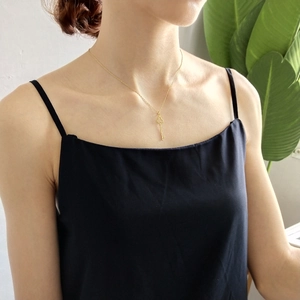 Detail of a gold clover key pendant necklace worn by a model against a plant background