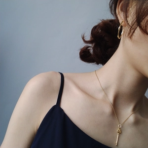 Detail of elegant gold key pendant necklace and classic hoop earrings on model