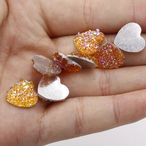 Detailopname van 12mm sprankelende oranje hars hartvormige cabochons op een hand