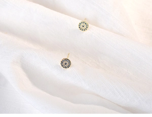 Macro shot of gold Evil Eye stud earrings with blue and white crystals on linen