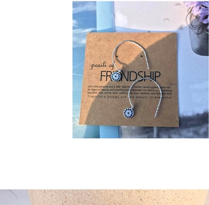 Detail view of silver evil eye drop earrings with blue rhinestones on a friendship card
