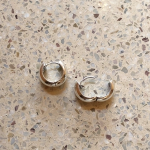 Macro shot of polished 925 sterling silver geometric thick hoop earrings on stone