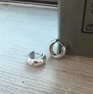 Detail view of 925 sterling silver wide hoop earrings on a minimalist wooden surface