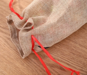 Detail of burlap wine gift bag with red satin drawstring on a wooden surface