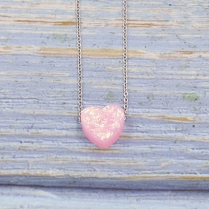 Macro detail of a sparkling pink heart-shaped opal pendant on a silver metal chain