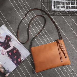 Brown PU leather crossbody envelope bag with tassel detail on a striped rug background