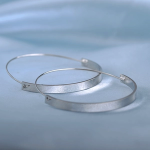 Polished silver geometric hoop earrings lying on soft blue silk fabric background