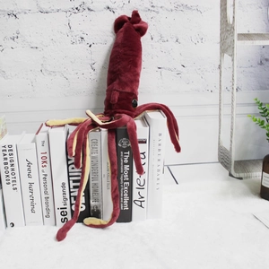 Deep red squid plush toy with yellow tentacles on a bookshelf in a bright room