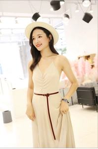 Close-up of a slim reddish-brown leather belt on a beige dress with a straw hat