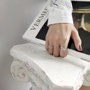 Close-up of minimalist silver chain ring and wide band ring worn on hand over art book
