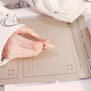 Close-up of strawberry enamel ring with red accents on a hand in a soft setting